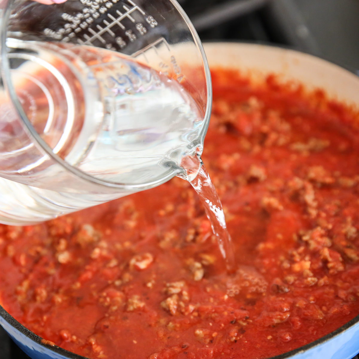 pouring water into a pot of meat and tomato product