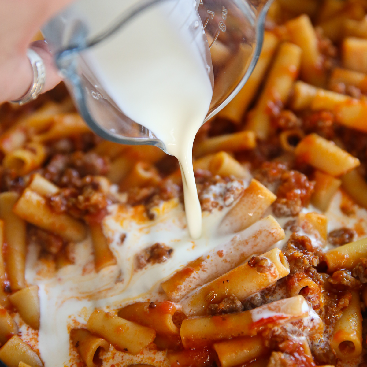 pouring cream into a pan of Skillet Baked Ziti from Our Best Bites