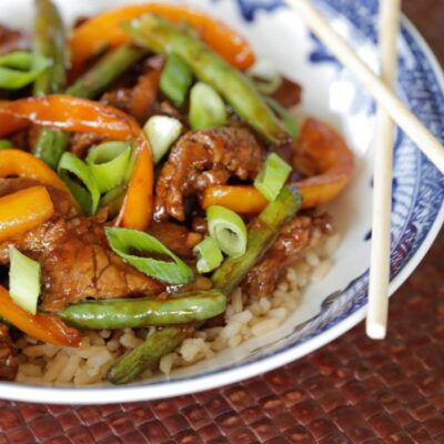 A blue and white dish with chopsticks, filled with rice and beef and green stir fry.