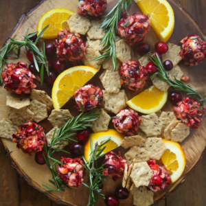 Cranberry-Orange goat cheese bites on a wooden tray with rosemary, orange, and crackers