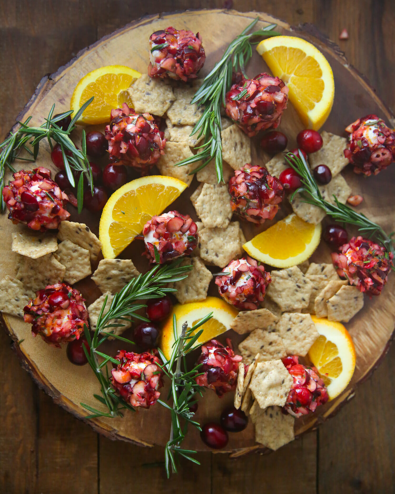 Cranberry-Orange goat cheese bites on a wooden tray with rosemary, orange, and crackers