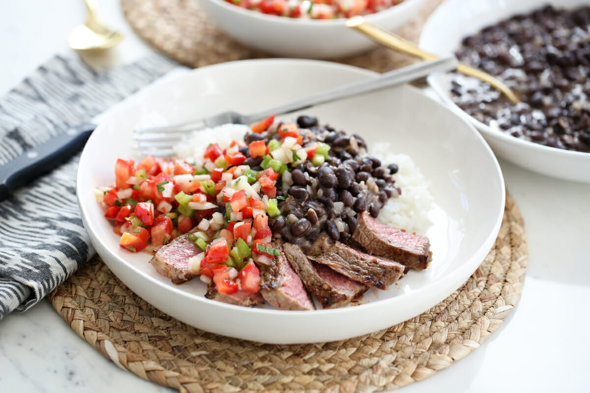 chopped tomato mixture with rice, beans, and steak on a white plate