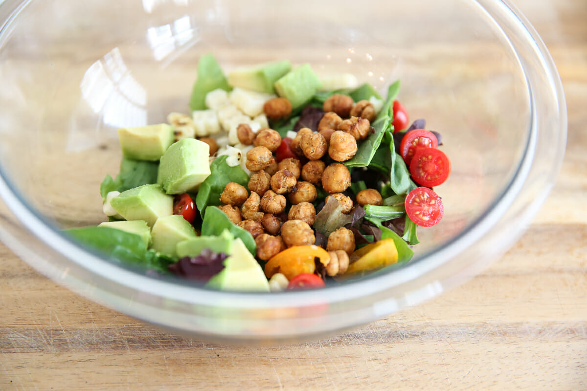 Fresh vegetables and roasted chickpeas in a clear bowl.