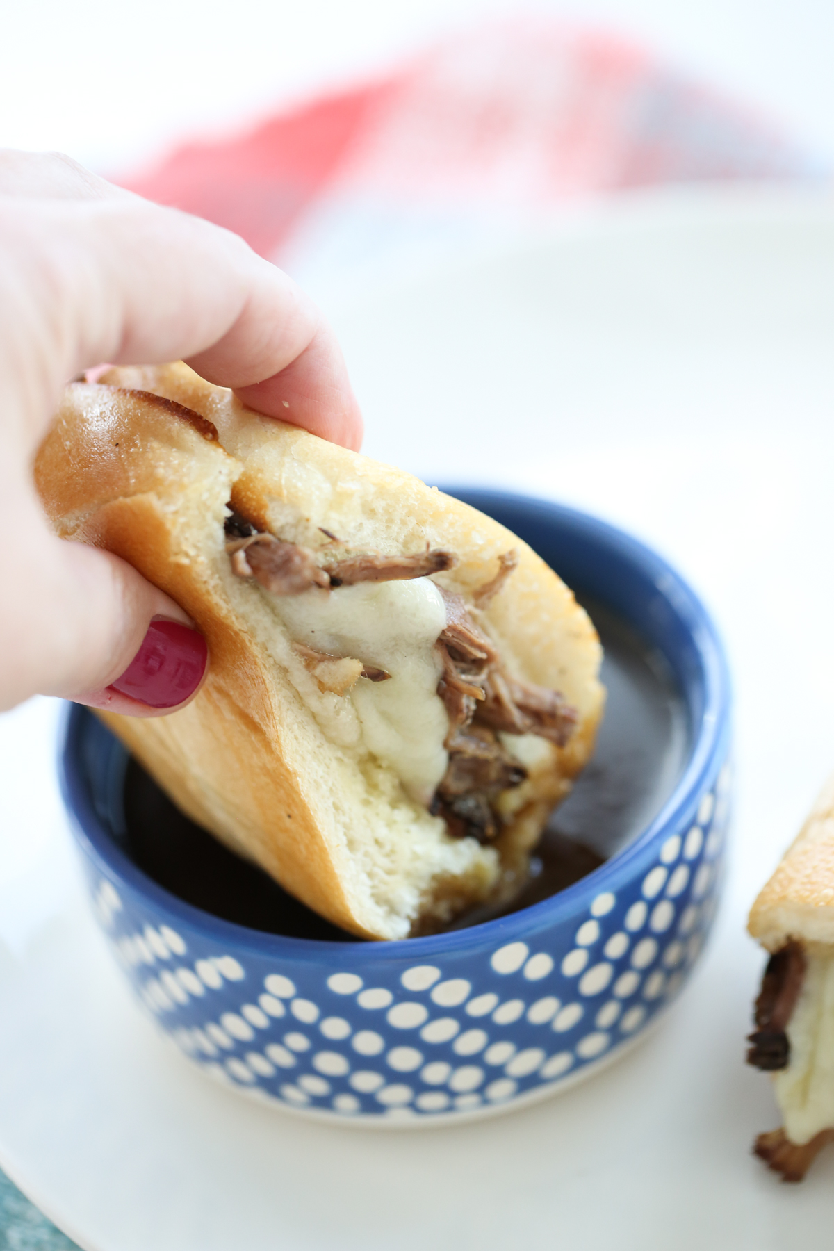 A sandwich with beef and cheese being dipped in au jus.