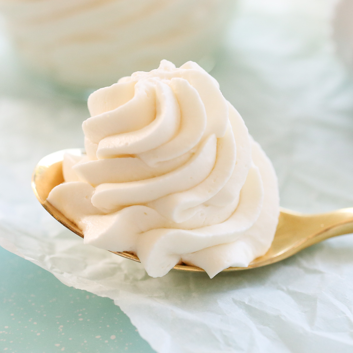 Whipped cream frosting piped onto a spoon that is resting on parchment paper.