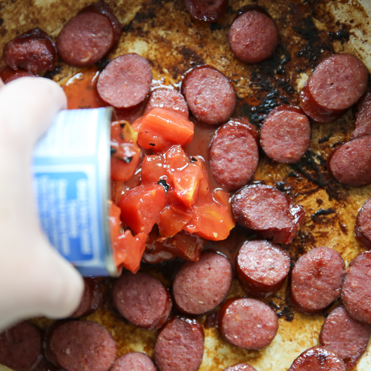 pouring a can of tomatoes into a skillet
