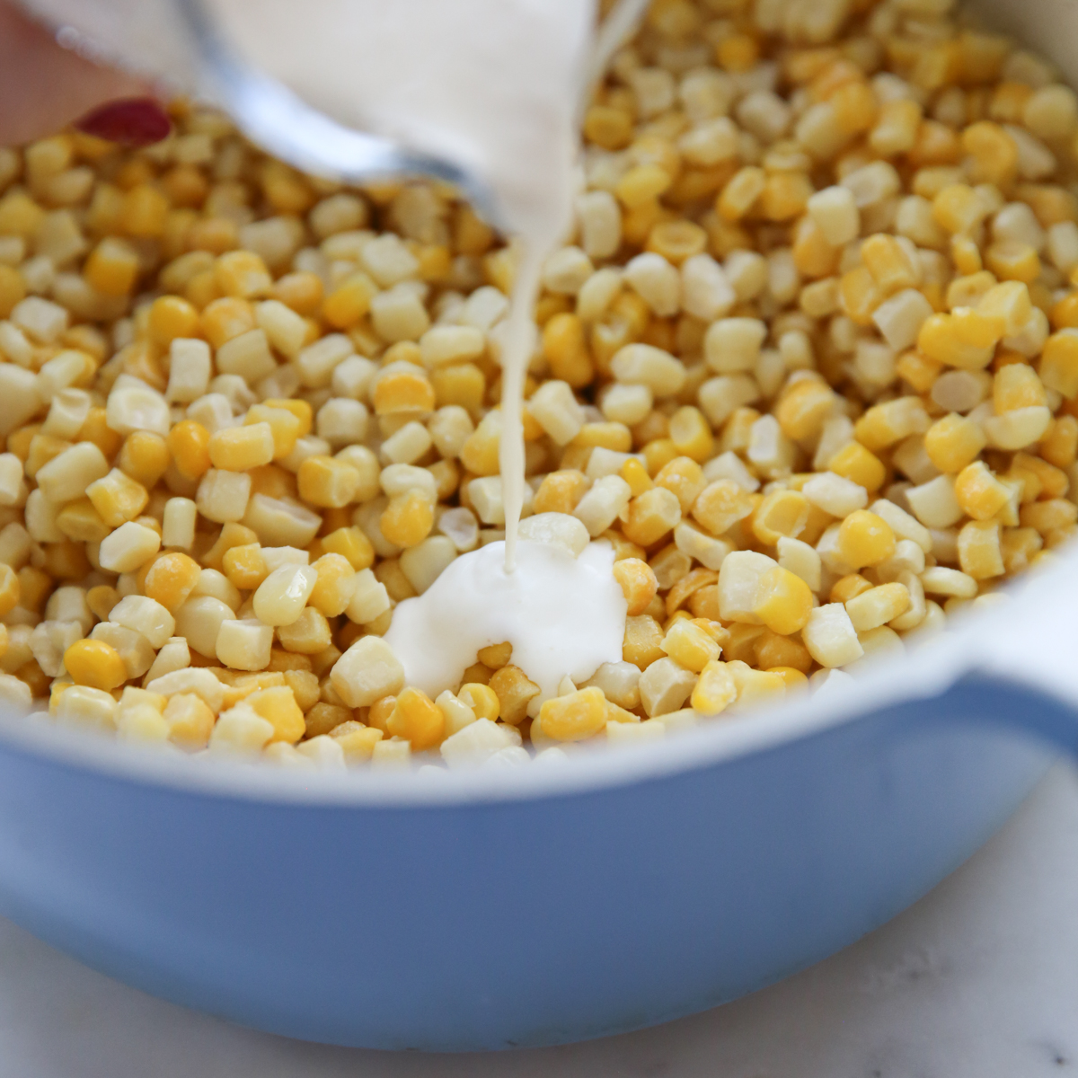 pouring cream into pot of corn