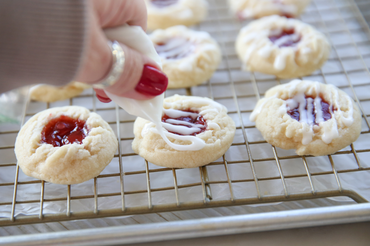 drizzling icing on raspberry thumbprint cookies