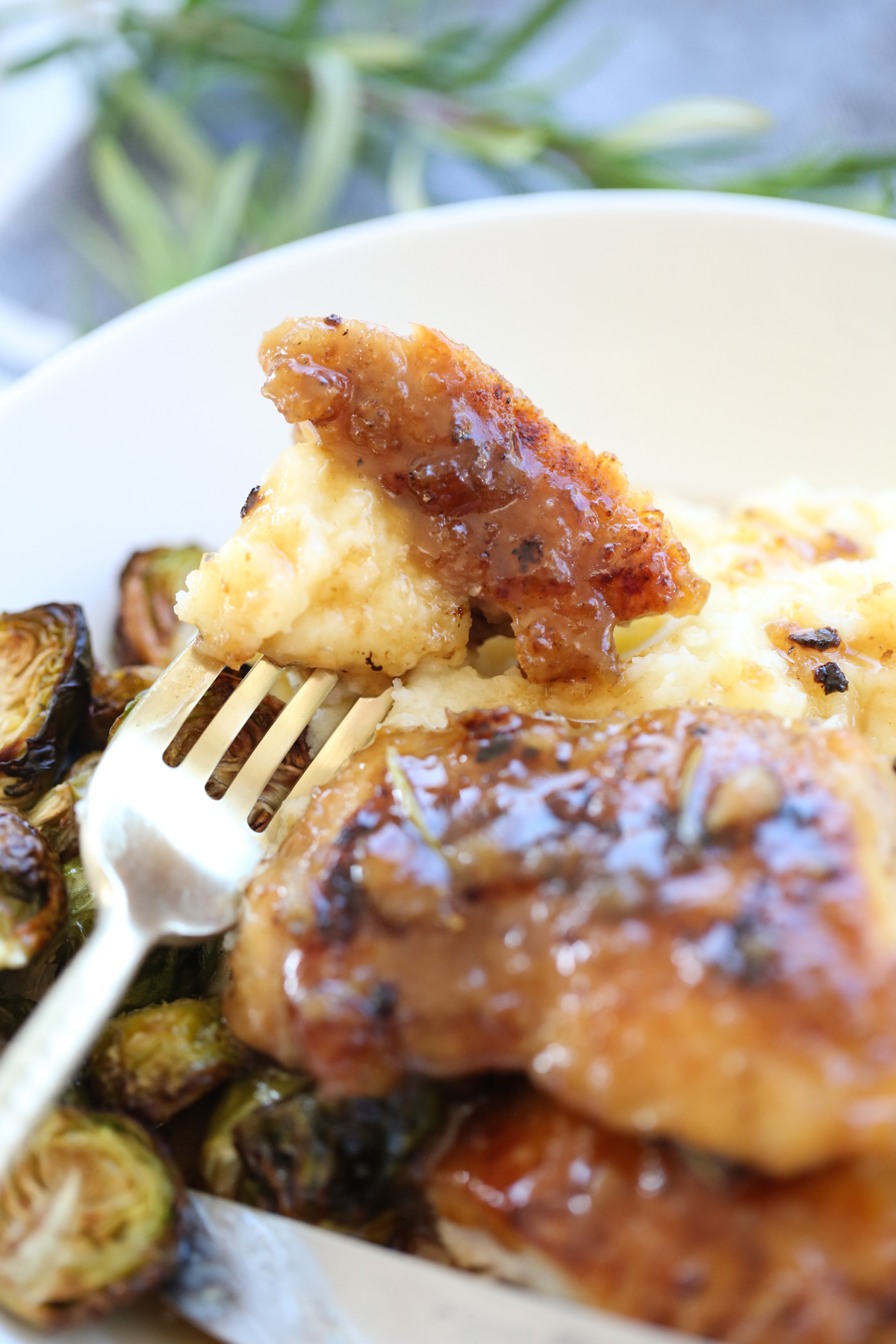 glazed chicken thighs on a serving plate with potatoes and brussells sprouts