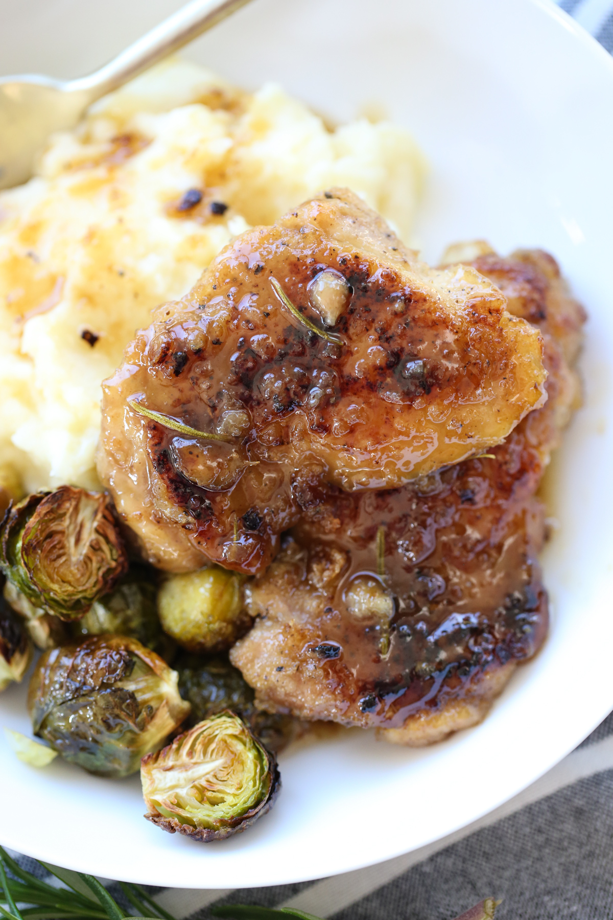 glazed chicken thighs on a serving plate with potatoes and brussells sprouts
