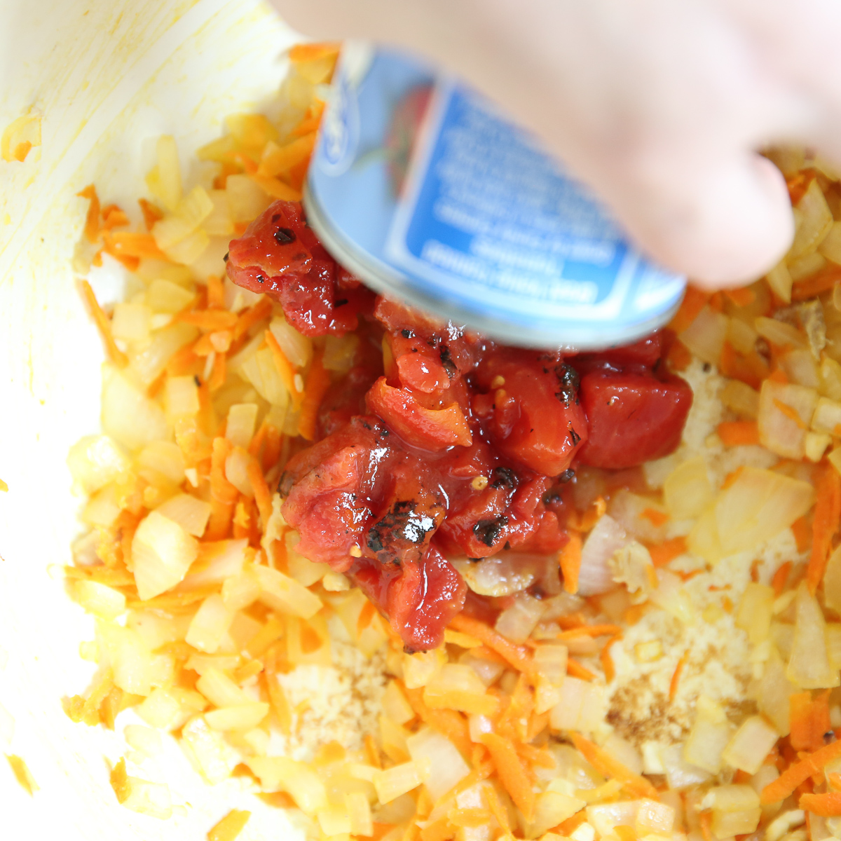 A can of tomato sauce is added to sautéed onions.