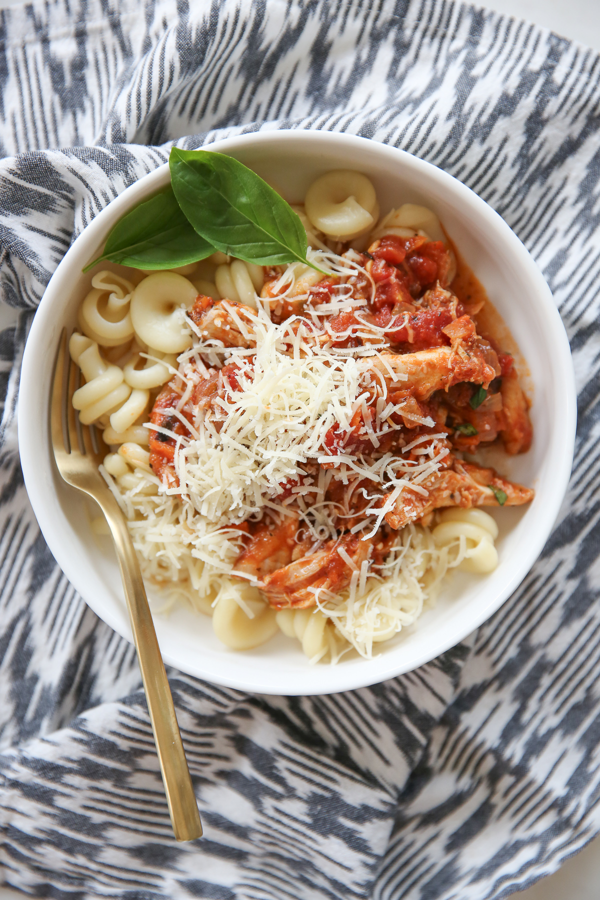 Braised Italian Chicken with pasta in a bowl with fresh basil.