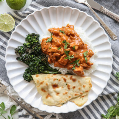 Butter chicken over rice with flatbread and broccoli, on a white plate