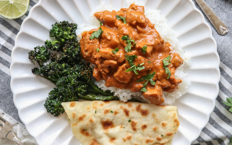 Butter chicken over rice with flatbread and broccoli, on a white plate