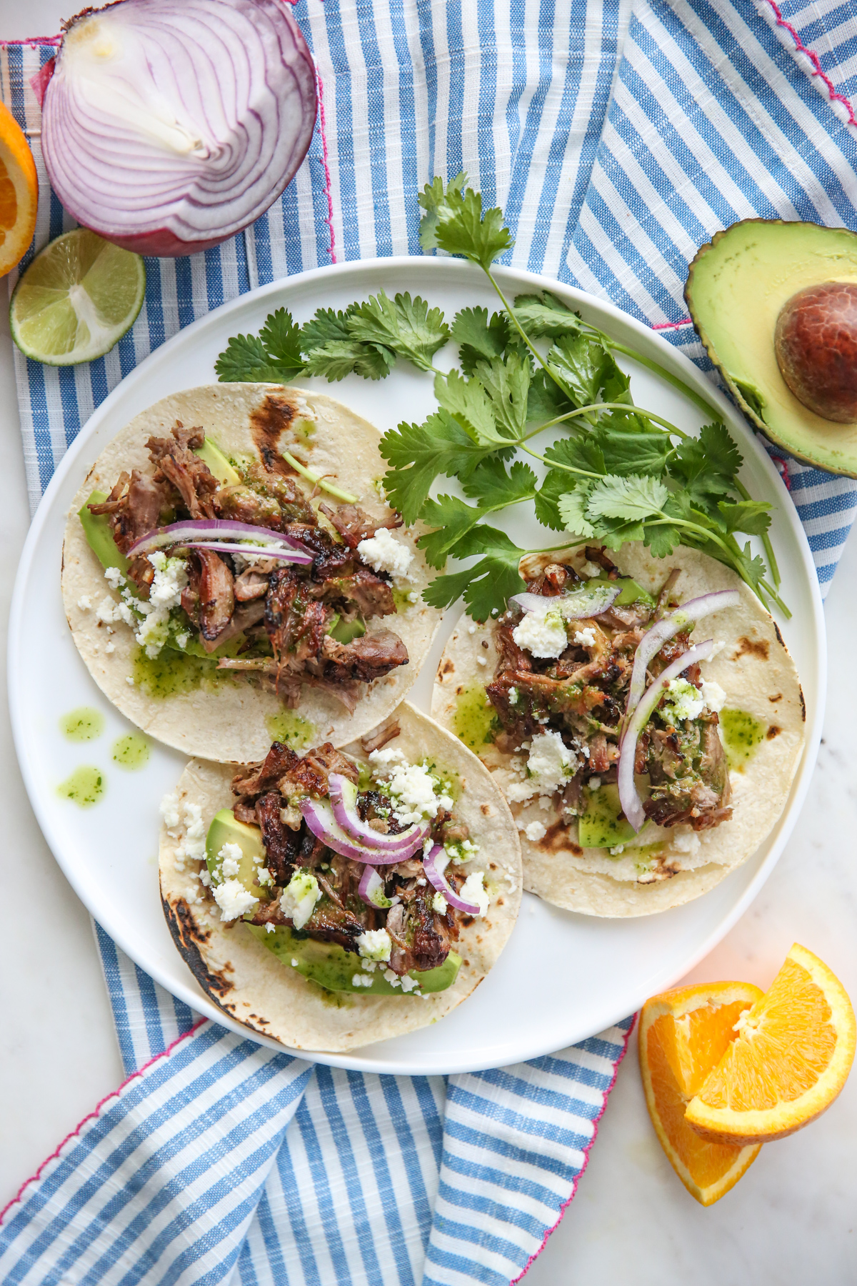a white plate full of carnitas with cheese, onions, and cilantro