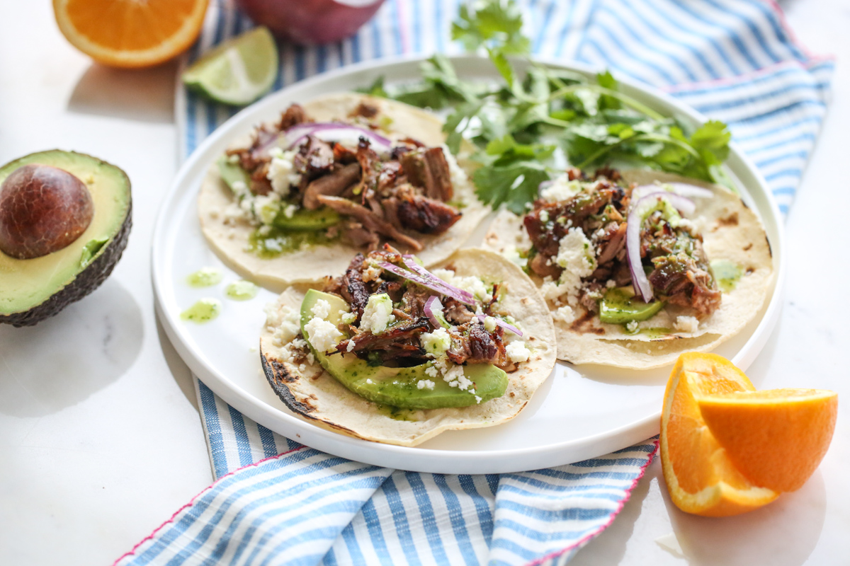 a white plate full of carnitas with cheese, onions, and cilantro