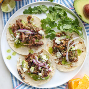 a white plate full of carnitas with cheese, onions, and cilantro