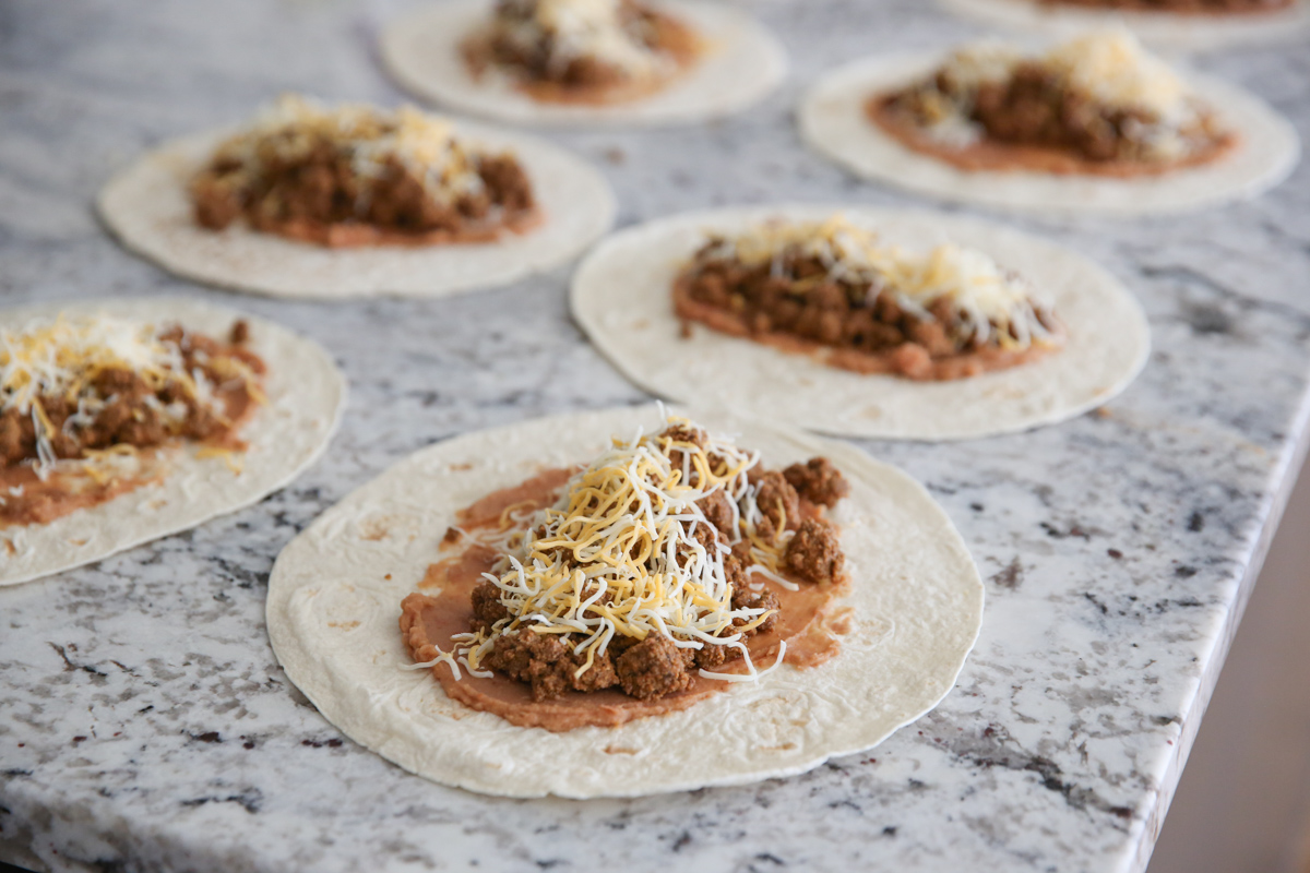 tortillas being filled with bean, meat, and cheese