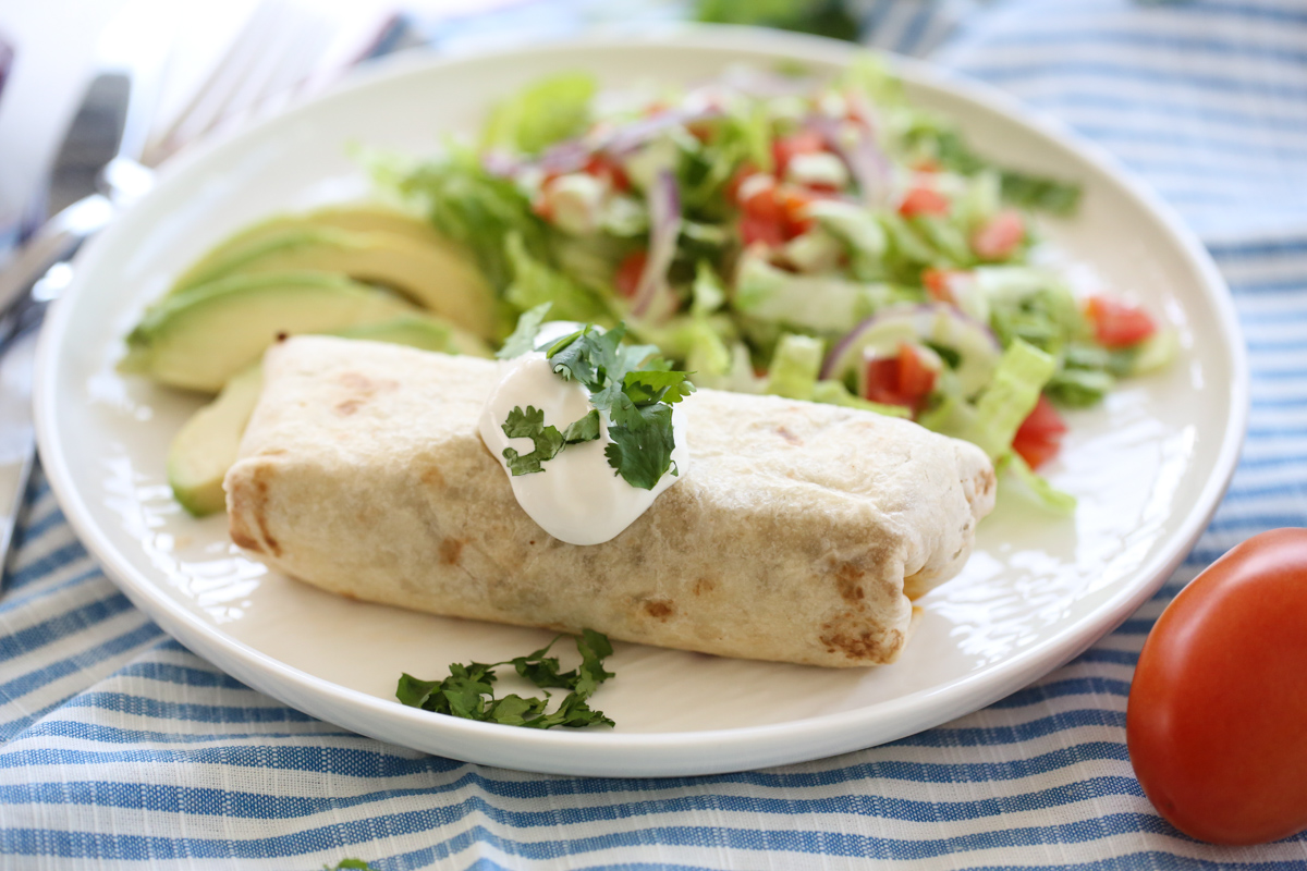 styled burrito on a white plate with sour cream on top