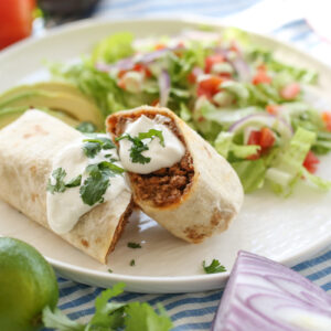 burrito on a white plate cut in half stuffed with bean, beef, and cheese.