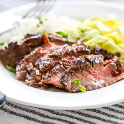 Sliced Ginger Soy Flank Steak on a plate with rice and cabbage