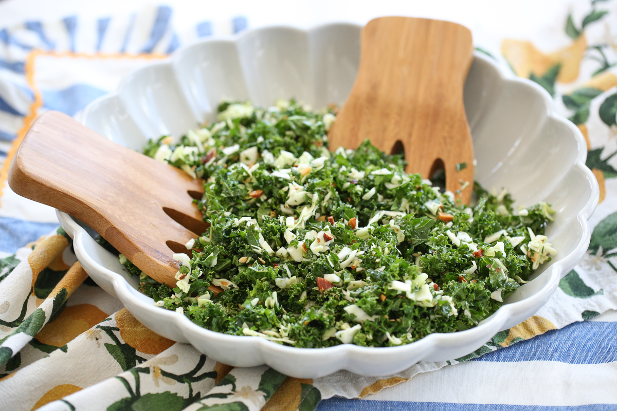 Kale crunch salad in a white serving bowl with salad tongs