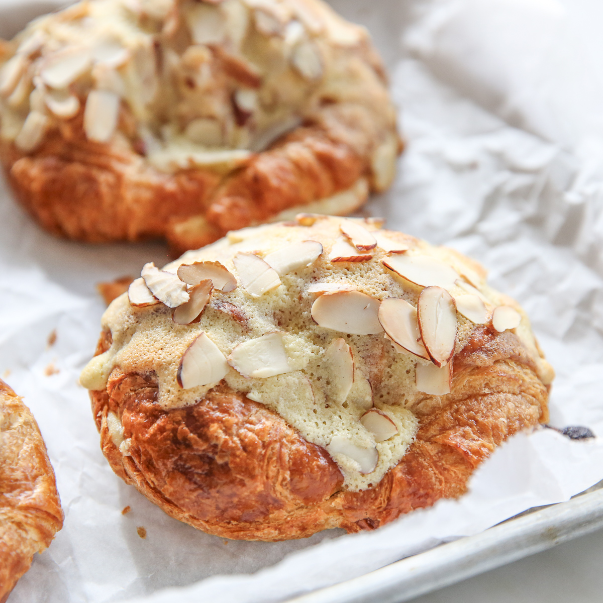 croissants on a baking sheet covered with almond cream and sliced almonds
