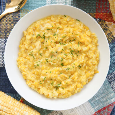 Bowl of creamed corn on a set table with chives on top