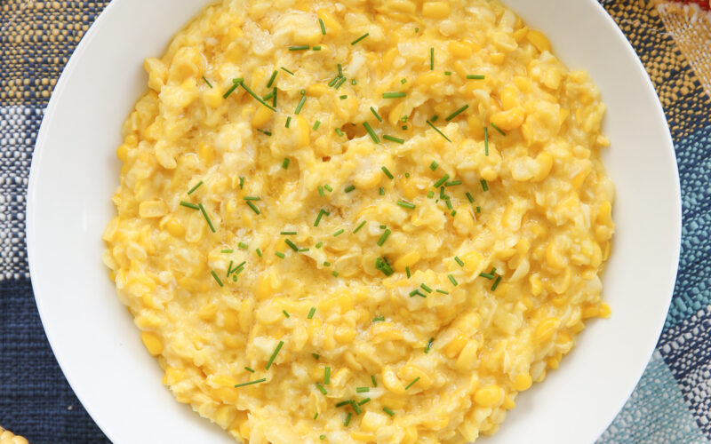 Bowl of creamed corn on a set table with chives on top