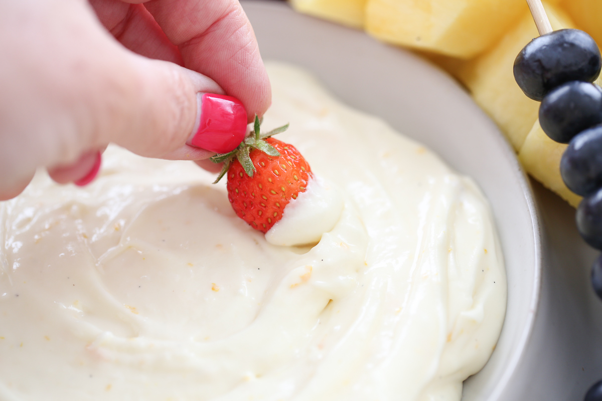 hand dipping a strawberry into fruit dip