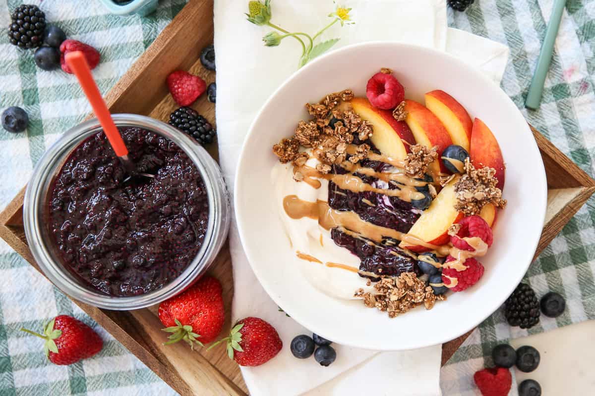 glass jar of chia seed jam next to a bowl of yogurt