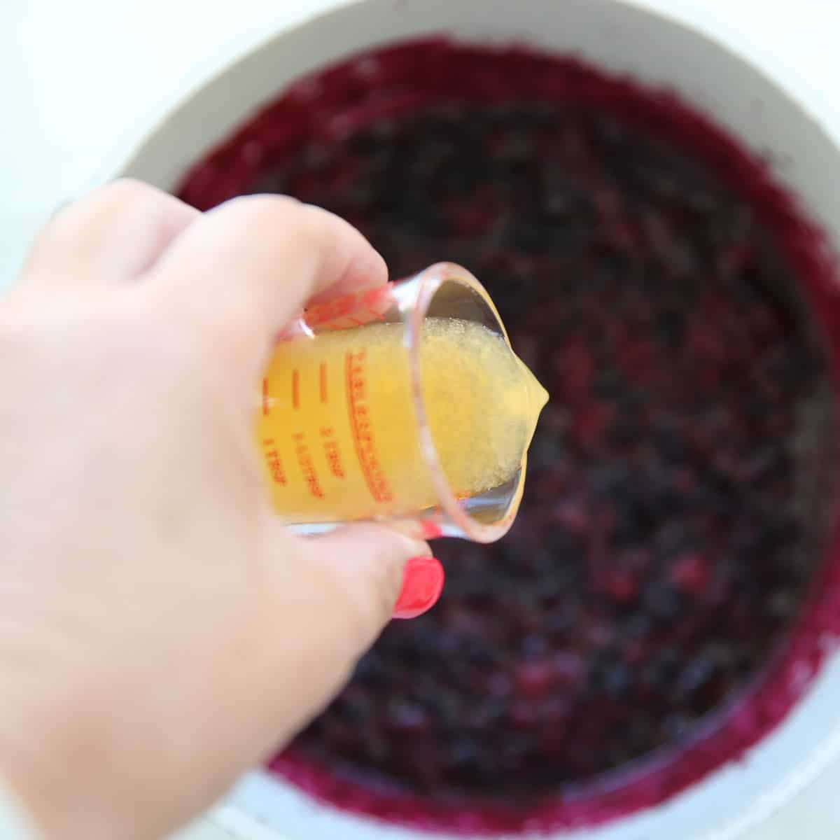 orange juice being poured into a pot of fruit