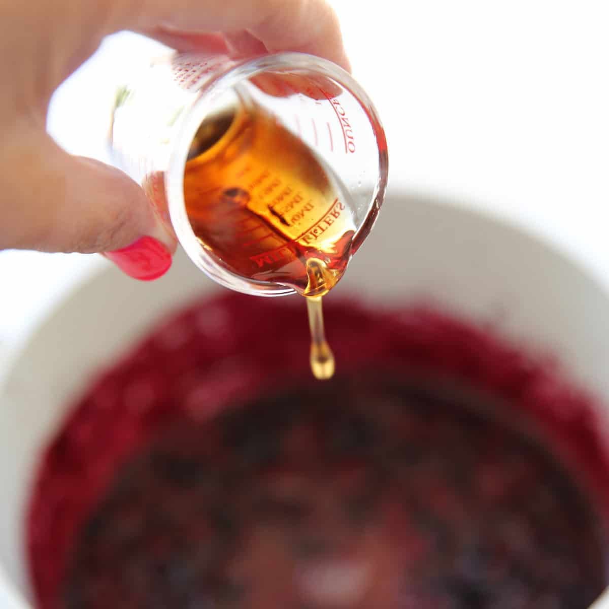 maple syrup being poured out of a small measuring cup