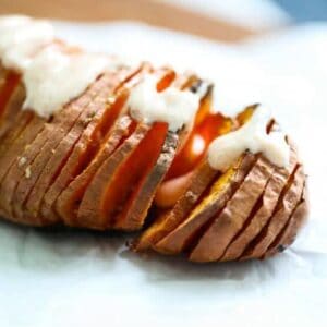 A hasselback sweet potato resting on a plate, with a creamy sauce drizzled over the top.