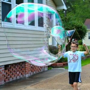 A boy making a giant bubble with two poles and string.