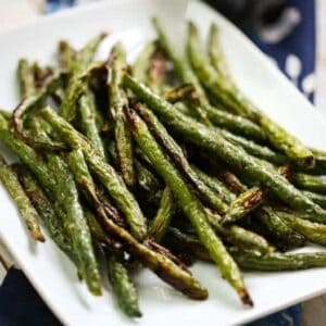 A pile of crispy roasted green beans on a white plate.