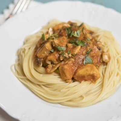 A pile of swirled spaghetti, topped with chicken cacciatore and garnished with fresh herbs.