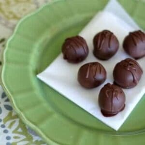 Six chocolate chip cookie dough truffles on green plate.