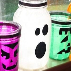 A row of spooky lanterns made by attaching colored tissue paper to mason jars with mod podge and adding funny paper faces.